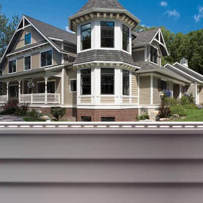 victorian-style-home-with-tan-vinyl-siding-sample A split image featuring a large Victorian-style house with tan siding, white trim, and a prominent octagonal turret on the top, and a close-up texture sample of tan horizontal vinyl siding on the bottom.