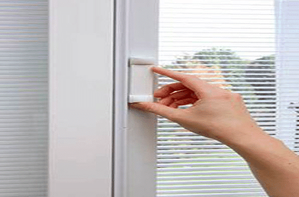 adjusting-magnetic-blind-slider A close-up of a person's hand using a white magnetic slider on the frame of a window with integrated blinds to raise or lower them.