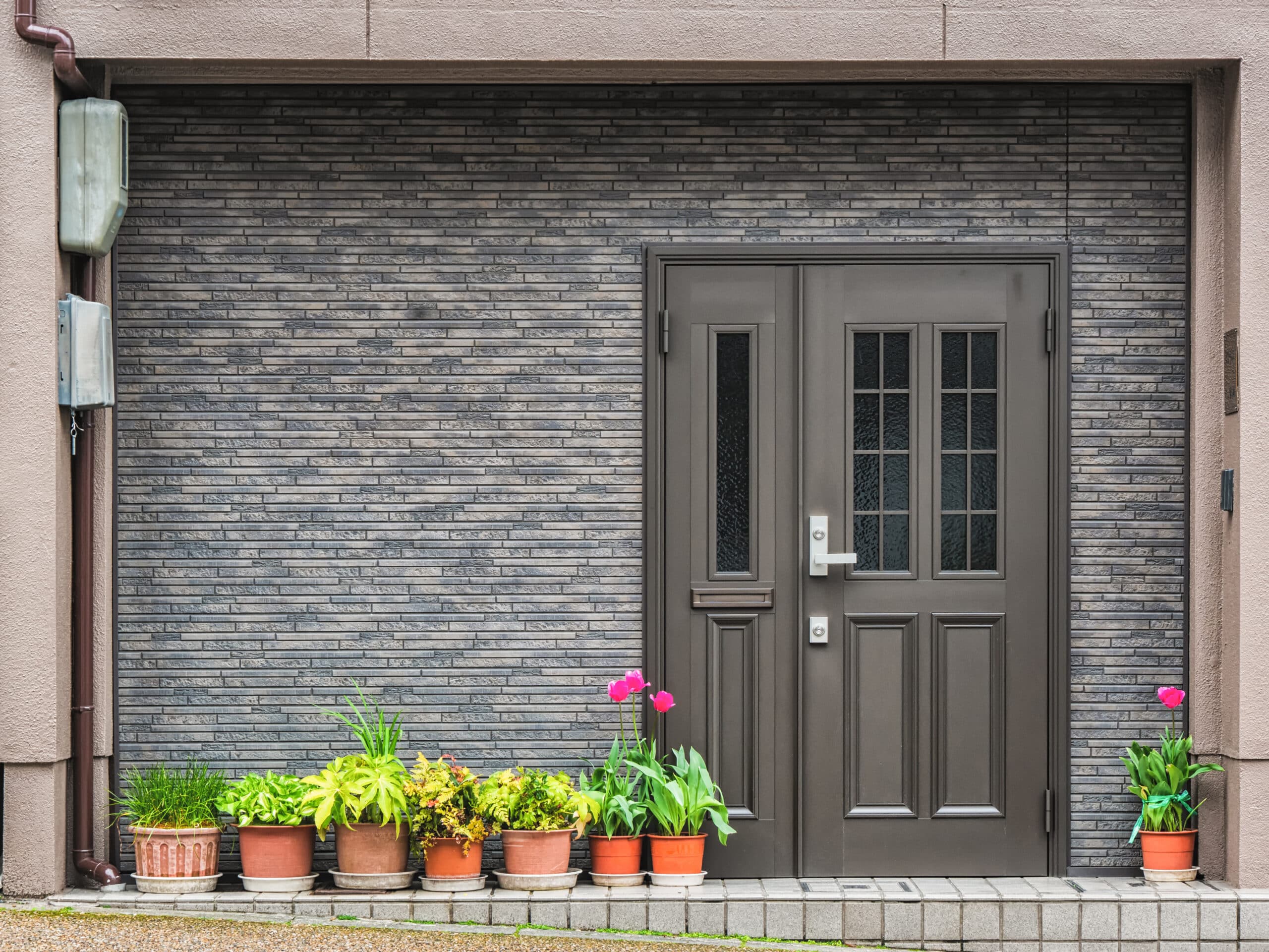 Gray front door with small square decorative windows and flower pots in fron of it Gray front door