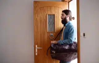 Young hipster man with bag entering front door when coming back home.