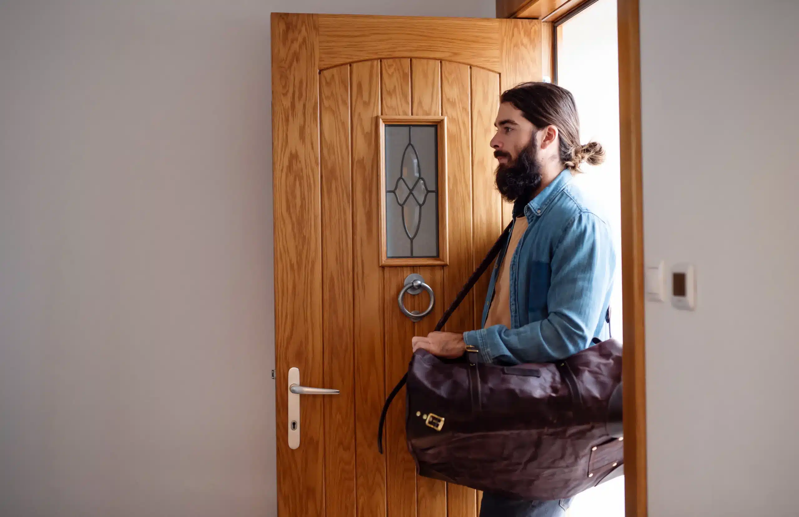 Young hipster man with bag entering front door when coming back home. Young hipster man with bag entering front door when coming back home.